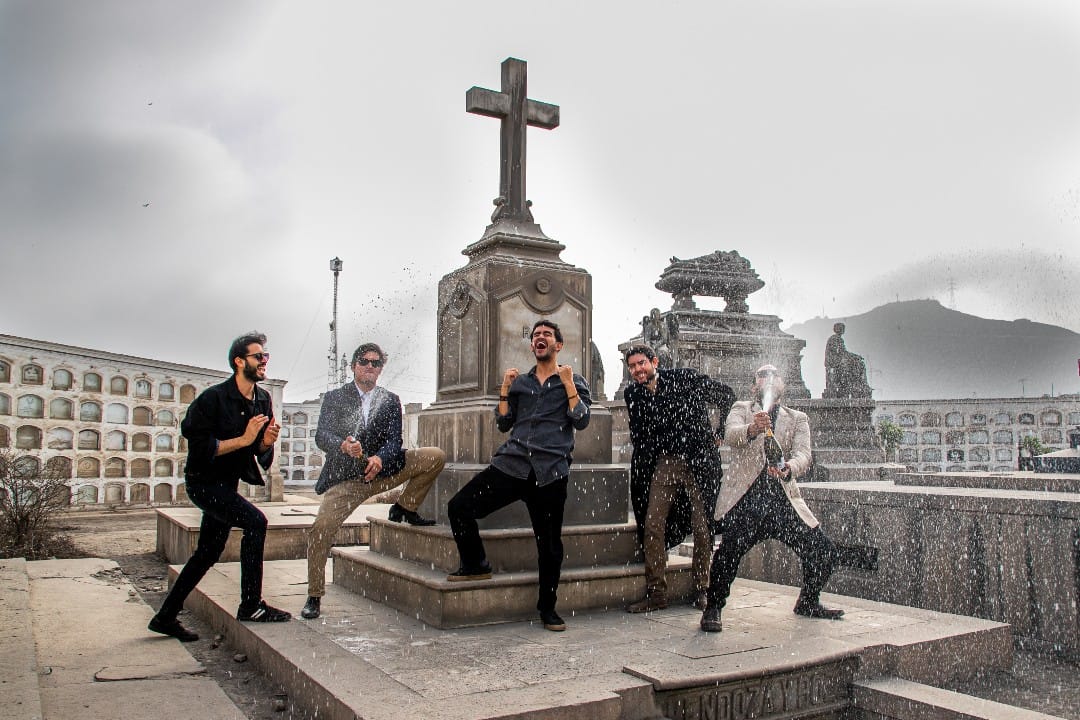 La banda peruana Perros Santos sosteniendo botellas de champagne en un cementerio de Lima