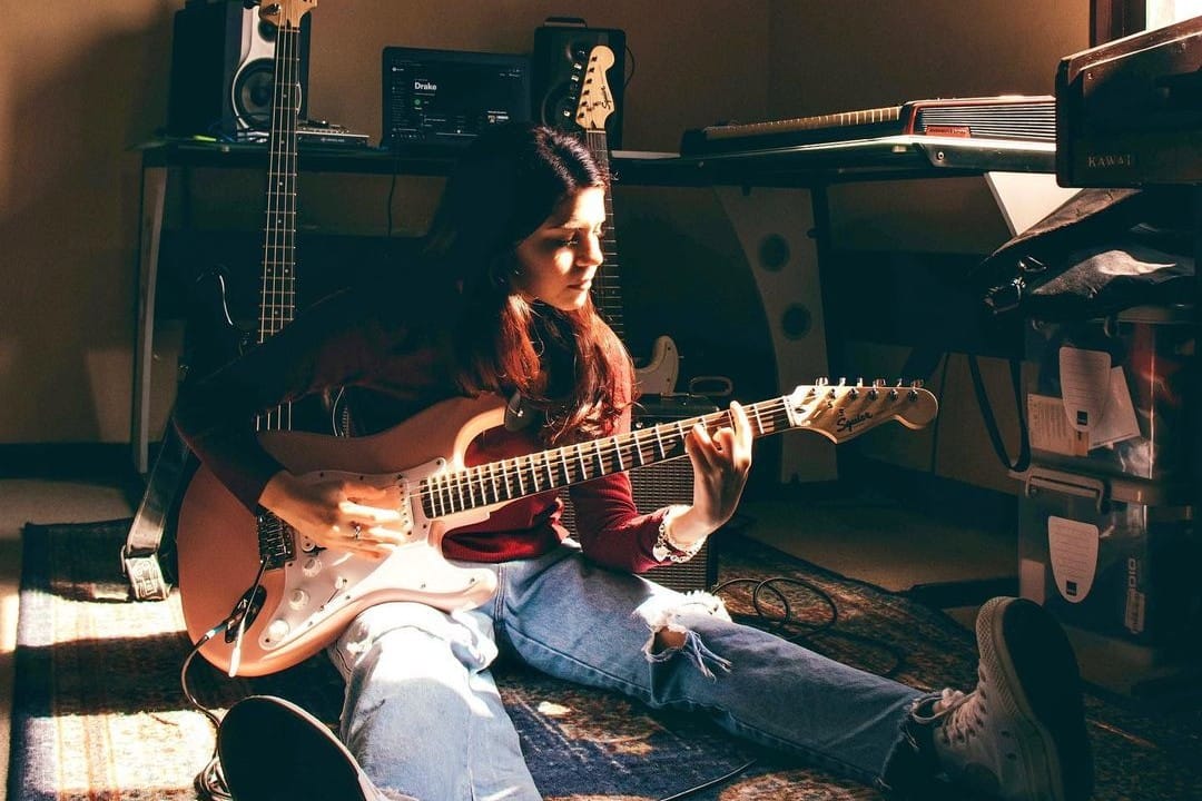 Rafaela Riboty sentada en el suelo de su estudio casero con una guitarra