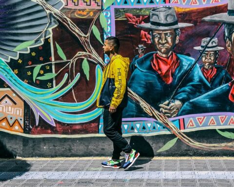 Liberato Kani caminando frente a un mural con motivos andinos