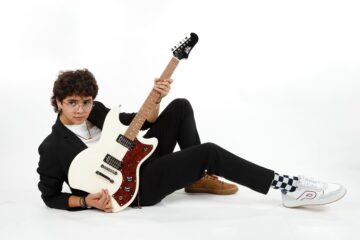 Luis Sosa recostado en el suelo con su guitarra en la mano