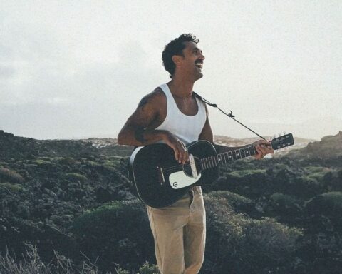 Good Franco sosteniendo una guitarra a la orilla del mar