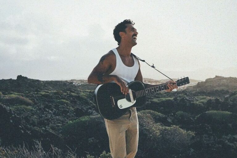 Good Franco sosteniendo una guitarra a la orilla del mar