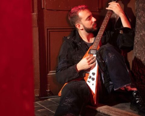 La Guarida del Dragón sentado sosteniendo su guitarra Flying V