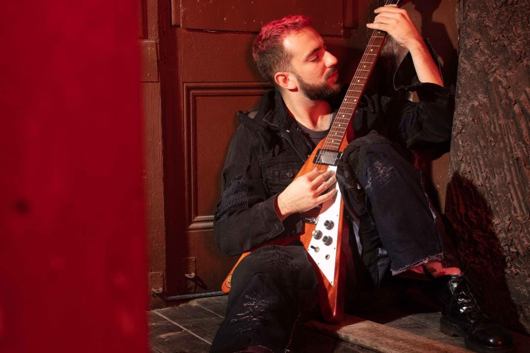 La Guarida del Dragón sentado sosteniendo su guitarra Flying V