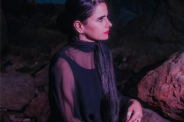 Sofia Kourtesis con un traje negro sobre unas rocas