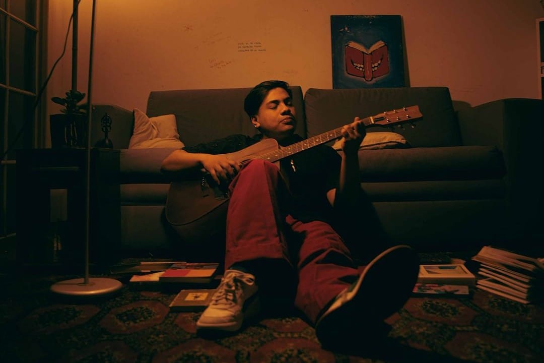 Tate tocando la guitarra sentado en su habitación