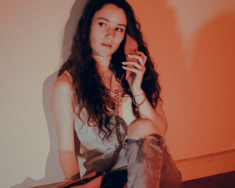 María Luz posando con un teléfono en la mano, sentada y apoyada en la pared