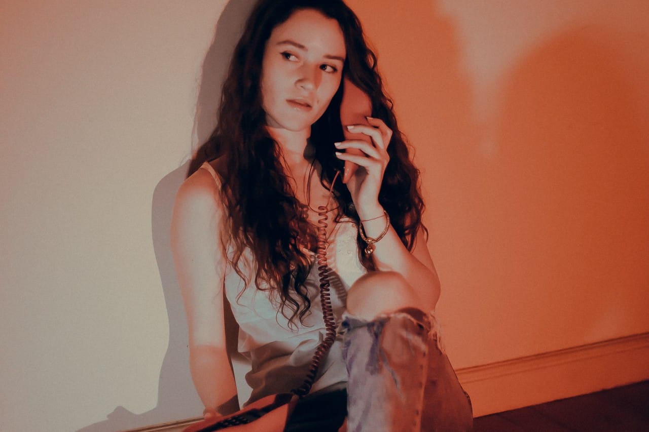 María Luz posando con un teléfono en la mano, sentada y apoyada en la pared