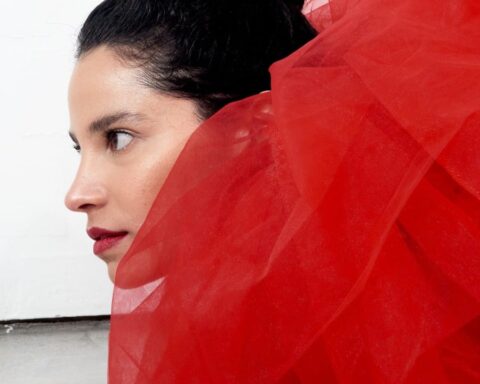 Fe Baca con un traje rojo mirando de perfil