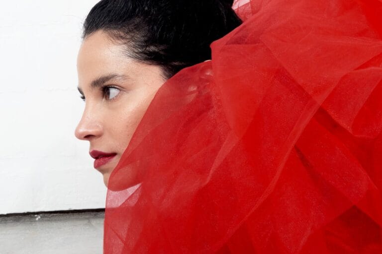 Fe Baca con un traje rojo mirando de perfil