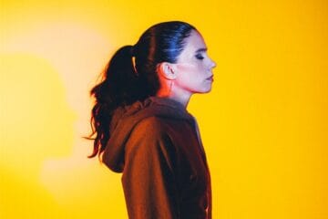 Javiera Mena posando de perfil con un fondo amarillo