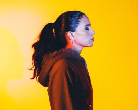 Javiera Mena posando de perfil con un fondo amarillo