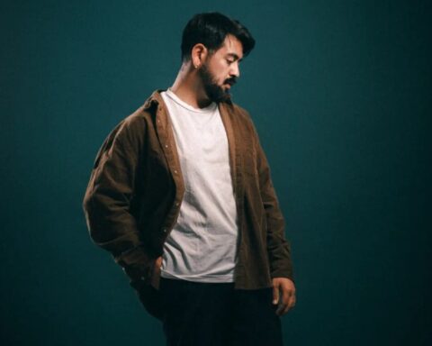 Nico Wang con polo blanco, chaqueta marrón y un fondo verde