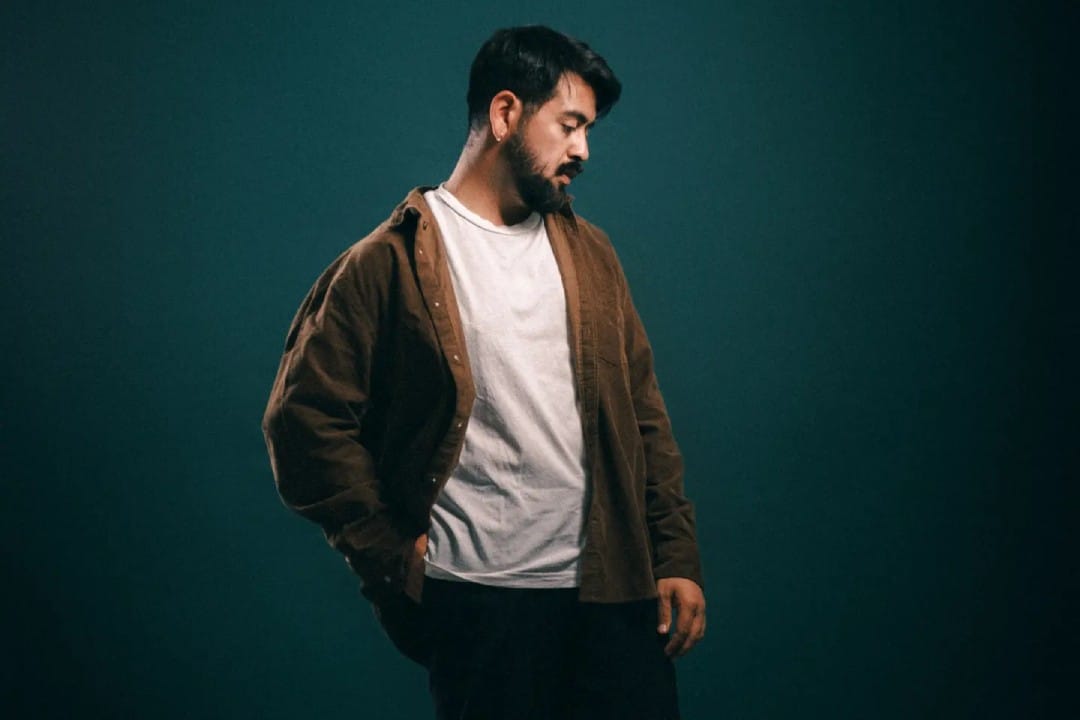 Nico Wang con polo blanco, chaqueta marrón y un fondo verde