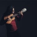 Brageiki de polo rojo tocando de pie su charango