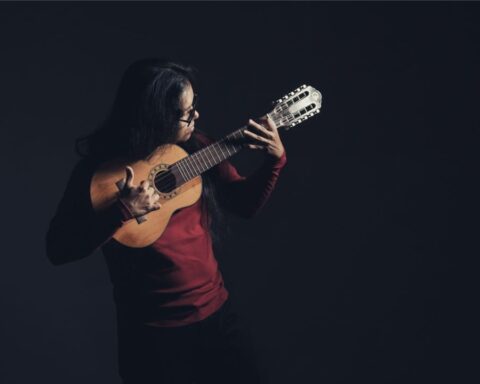 Brageiki de polo rojo tocando de pie su charango