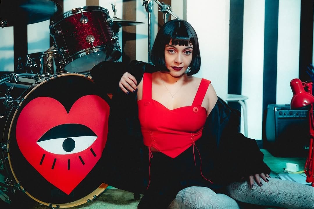 Cancamusa con blusa roja sentada al lado de la batería