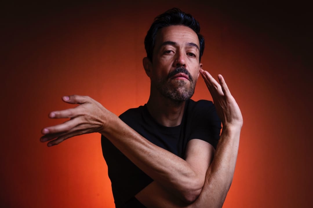 Meme del Real posando con polo negro sobre fondo rojo