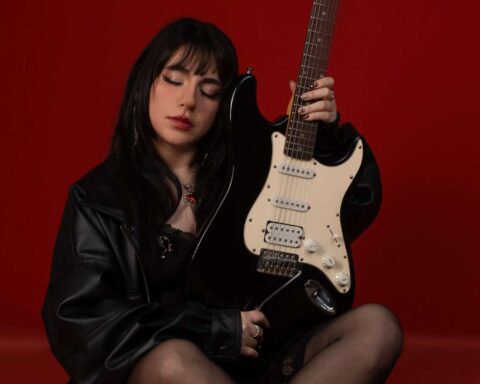 Roxie sosteniendo su guitarra en fondo rojo