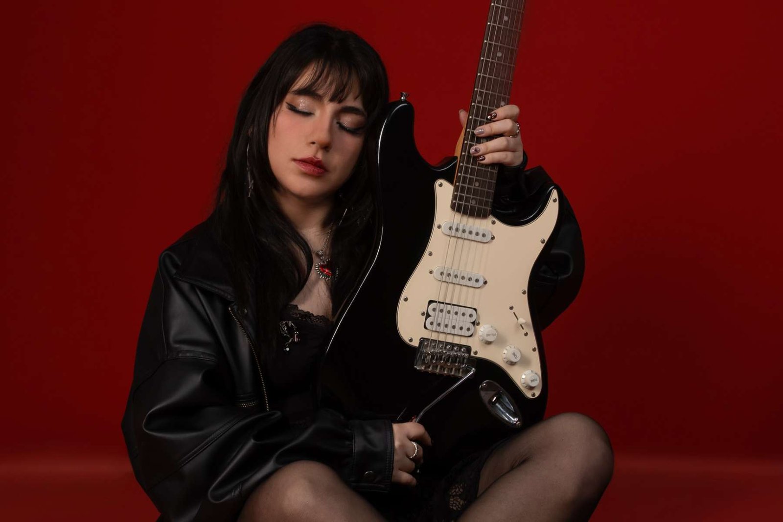 Roxie sosteniendo su guitarra en fondo rojo