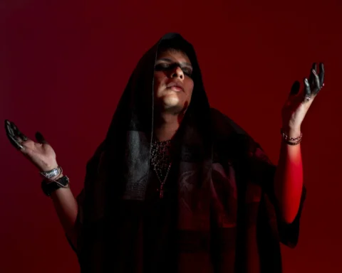 Alexander Goché con una capucha negra y las manos manchadas de negro, sobre un fondo rojo