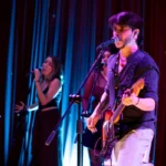 DEBRA en concierto, con un guitarrista y cantante frente al micrófono
