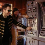 José Biggs y John Shepherd frente a una consola de transmisión, en una imagen del universo visual de “Algoritmos”