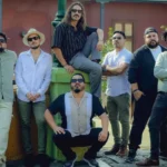 Los siete integrantes de Olaya Sound System posan junto a un farol de tres globos frente a una casona de balcones verdes