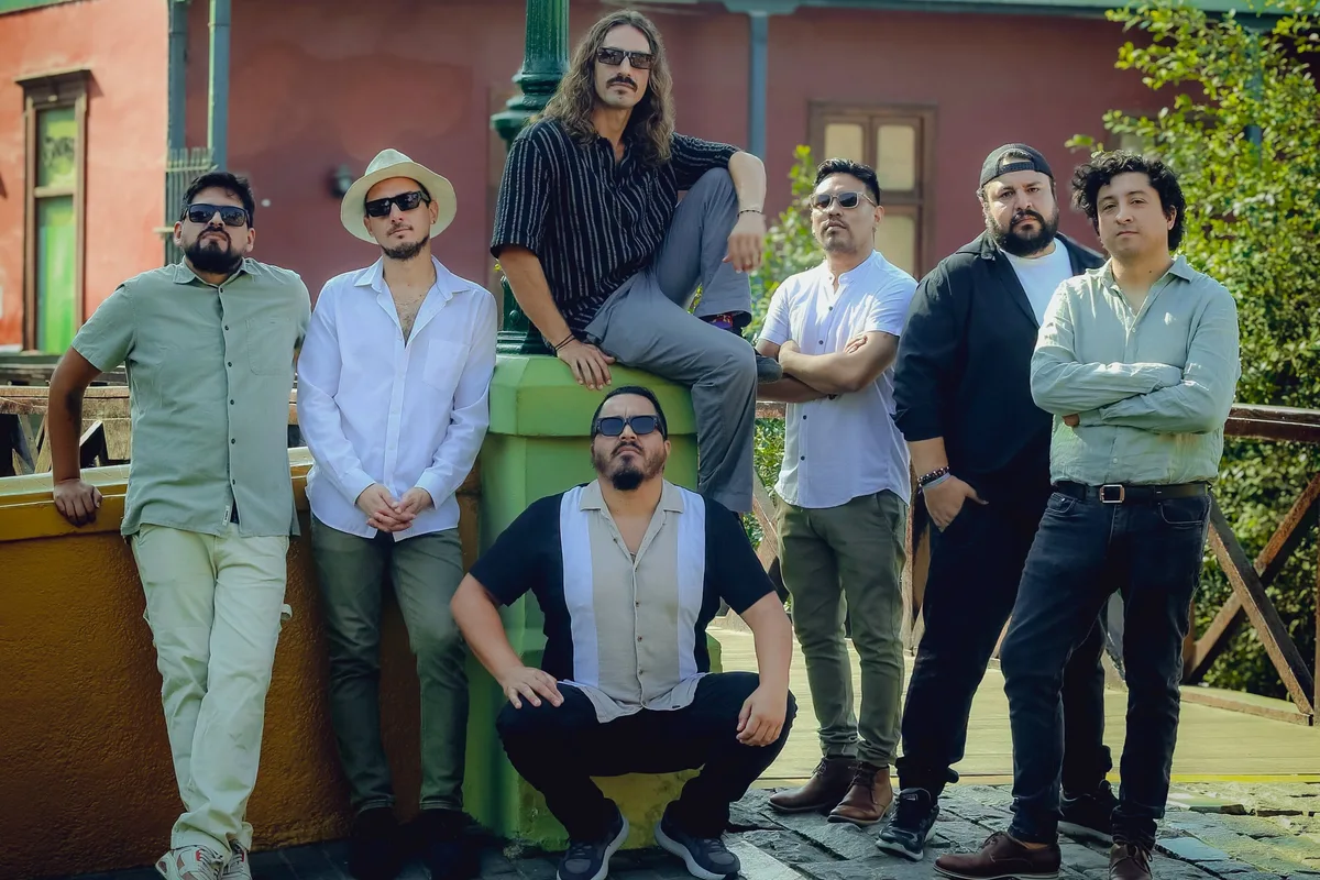 Los siete integrantes de Olaya Sound System posan junto a un farol de tres globos frente a una casona de balcones verdes